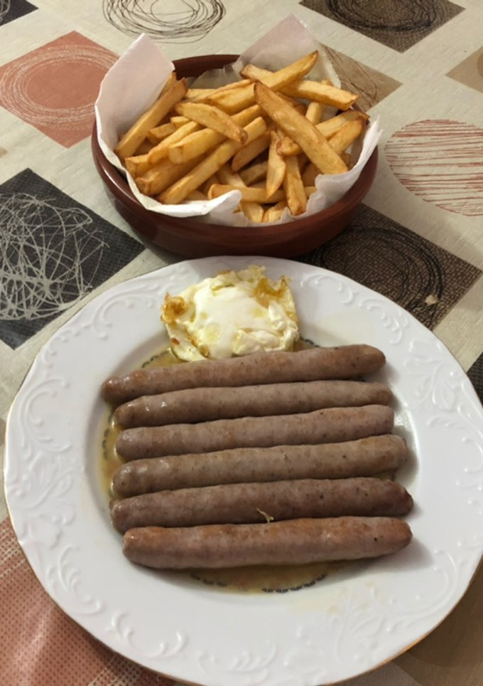 Una foto de Salchichas cocidas con vino patatas fritas y huevo frito