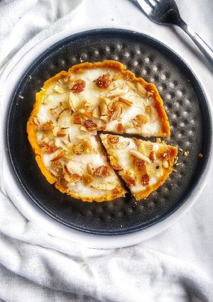 A picture of Besan laddoo tart filled with rice pudding topped with nuts.