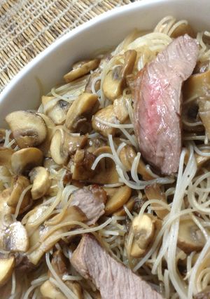 A picture of Blushing beef slices and mushrooms in rice noodles.