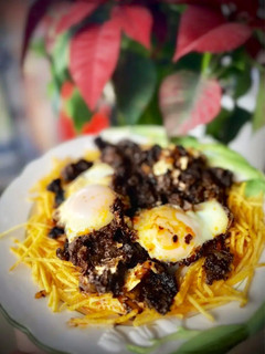 Una foto de Revuelto de morcilla de León con sofrito de cebolla y pasas sobre cama de patatas paja