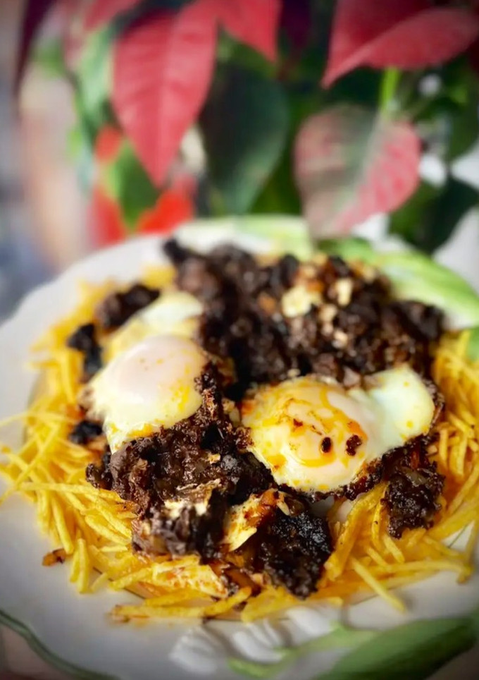Una foto de Revuelto de morcilla de León con sofrito de cebolla y pasas sobre cama de patatas paja