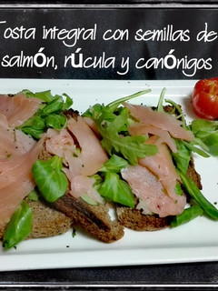 Una foto de Tosta integral con semillas de lino, salmón, rúcula y canónigos
