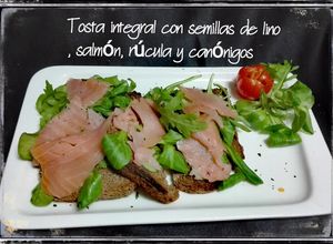 Una foto de Tosta integral con semillas de lino, salmón, rúcula y canónigos