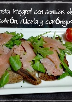 Una foto de Tosta integral con semillas de lino, salmón, rúcula y canónigos