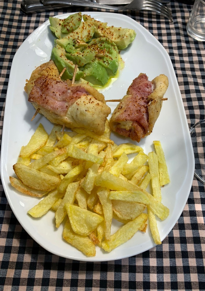 Una foto de Rollitos de pechuga de pollo, jamón York y foie acompañado de aguacate y patatas fritas