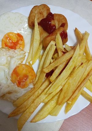 Una foto de Nuggets de pollo con un par de huevos fritos y papas