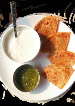 A picture of Aaloo pyaaz paratha with curd and garlic chutney.