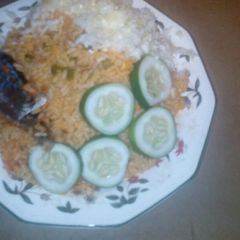 A picture of Jollof rice served fried fish, garnished with cucumba and cabbag.