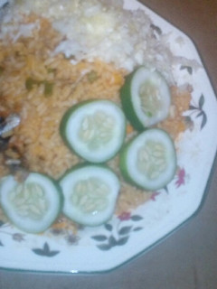A picture of Jollof rice served fried fish, garnished with cucumba and cabbag.