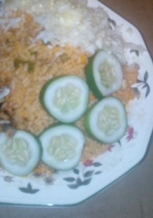 A picture of Jollof rice served fried fish, garnished with cucumba and cabbag.