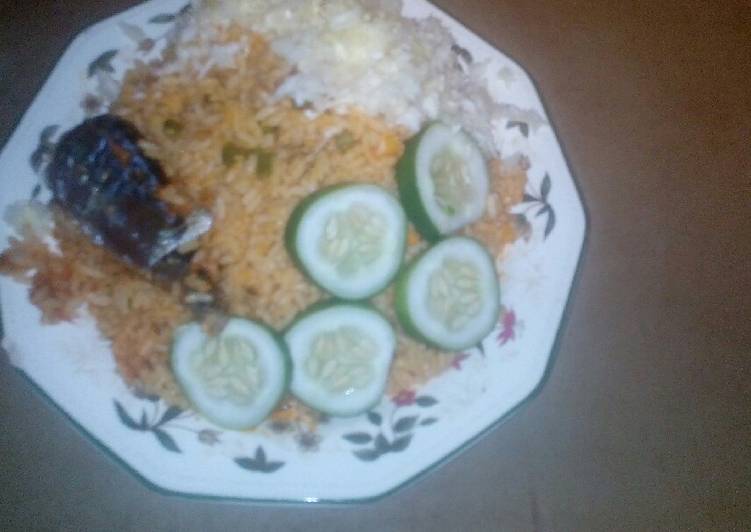 Jollof rice served fried fish, garnished with cucumba and cabbag