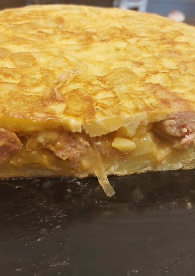 Una foto de Tortilla de patatas con salchichas encebollada al vino