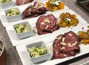 A picture of Smoked Rib-eye over Mustard Sauce, Loaded Smashed Potatoes, and Cucumber Salad.