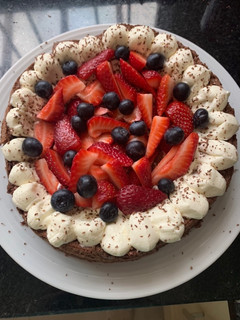 Una foto de Brownie con crema, frutillas y arándanos