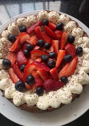 Una foto de Brownie con crema, frutillas y arándanos