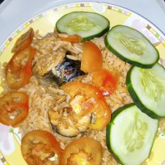 A picture of Jollof rice with sliced cucumbers and fresh tomatoes.