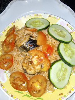 A picture of Jollof rice with sliced cucumbers and fresh tomatoes.