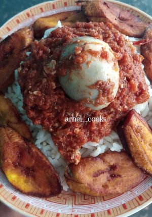 A picture of Rice, plantain, egg sauce and boiled egg.