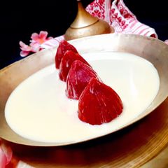 A picture of Beetroot Bhapa Pitha Stuffed With Coconut and Submerged In milkmaid.