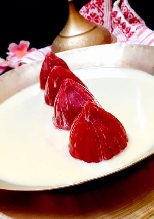 A picture of Beetroot Bhapa Pitha Stuffed With Coconut and Submerged In milkmaid.