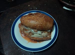 Una foto de Torta bañada en jitomate,  carnitas de cerdo con cebolla desflemada estilo las Correa de San Diego