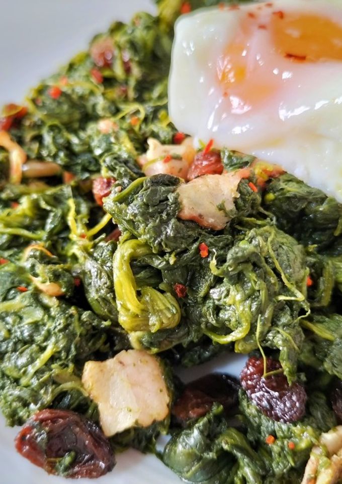 Una foto de Salteado trufado de espinacas con bacon, pasas, piñones y huevo poché