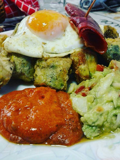 Una foto de Huevos rotos sobre alcachofas con salsa romesco y guacamole