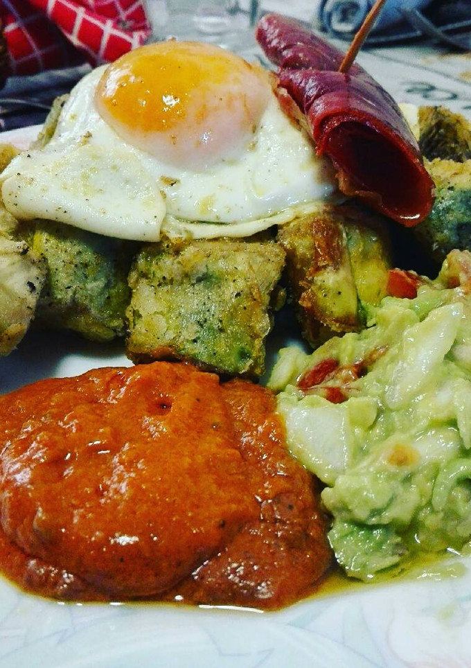Una foto de Huevos rotos sobre alcachofas con salsa romesco y guacamole