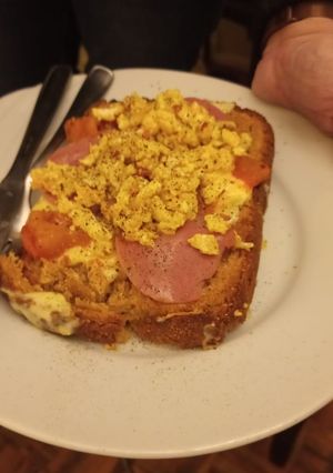 Una foto de Tostada de pan integral con revuelto de huevos, tomatitos cherry, panceta y queso provolone rallado