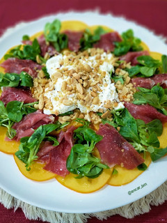 Una foto de Carpaccio de caqui con jamón ibérico, burrata y frutos secos