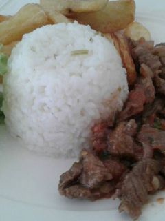 Una foto de Lomo salteado con una porción de arroz y papas fritas