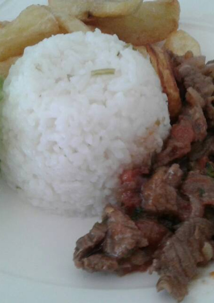 Una foto de Lomo salteado con una porción de arroz y papas fritas