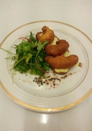 Una foto de Crostini de tomate y langostinos sobre colchón de hojas verdes