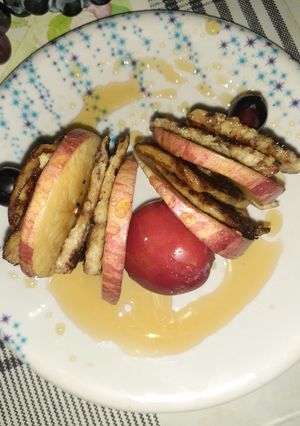 A picture of Banana pancake with apple and grapes sticks.