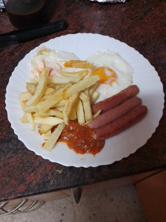 Una foto de Papas fritas con huevo frito, salchichas y salsa de tomate