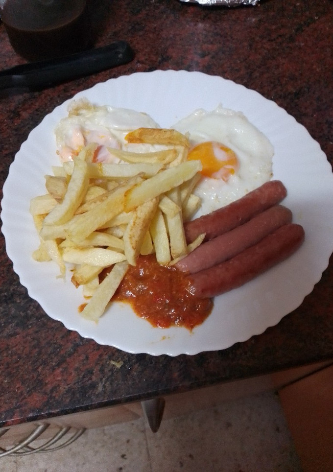 Una foto de Papas fritas con huevo frito, salchichas y salsa de tomate