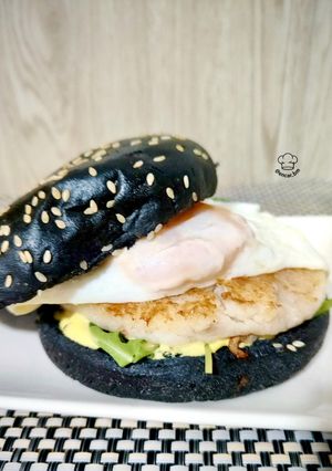 Una foto de Black burger de merluza y camarones con huevo frito y salsa de mango y curry