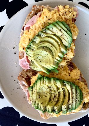 A picture of Scrambled eggs on olive bread, with bacon, mushroom and avocado 🥑.