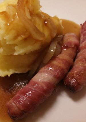 A picture of Pigs in blankets, mash and onion gravy.