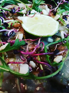 Una foto de Carpaccio de gambas, con rúcula, raíces de rábano y grana padano