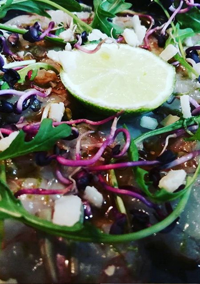 Una foto de Carpaccio de gambas, con rúcula, raíces de rábano y grana padano