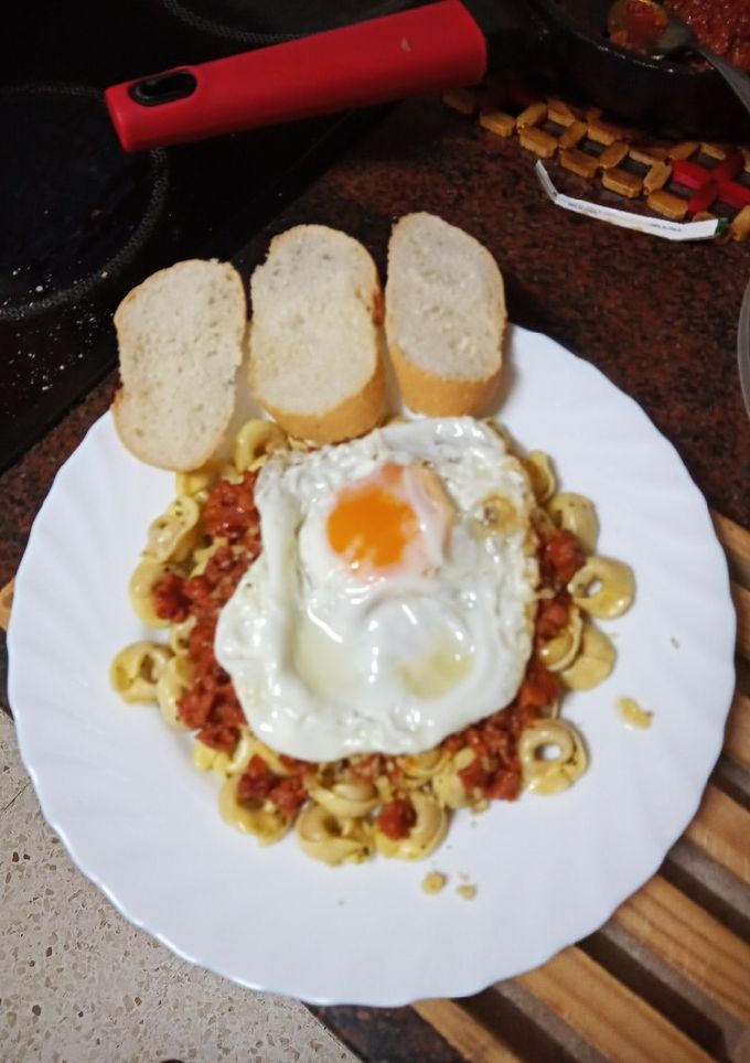 Una foto de Tortellinis con boloñesa de salchicha y chorizo y huevo frito