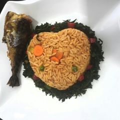 A picture of Jollof rice with vegetables and fried fish.