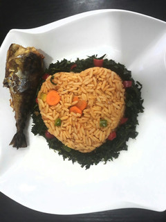 A picture of Jollof rice with vegetables and fried fish.