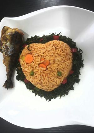 A picture of Jollof rice with vegetables and fried fish.