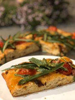 Una foto de Focaccia de cebolla y tomates cherry con rúcula