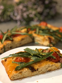 Una foto de Focaccia de cebolla y tomates cherry con rúcula