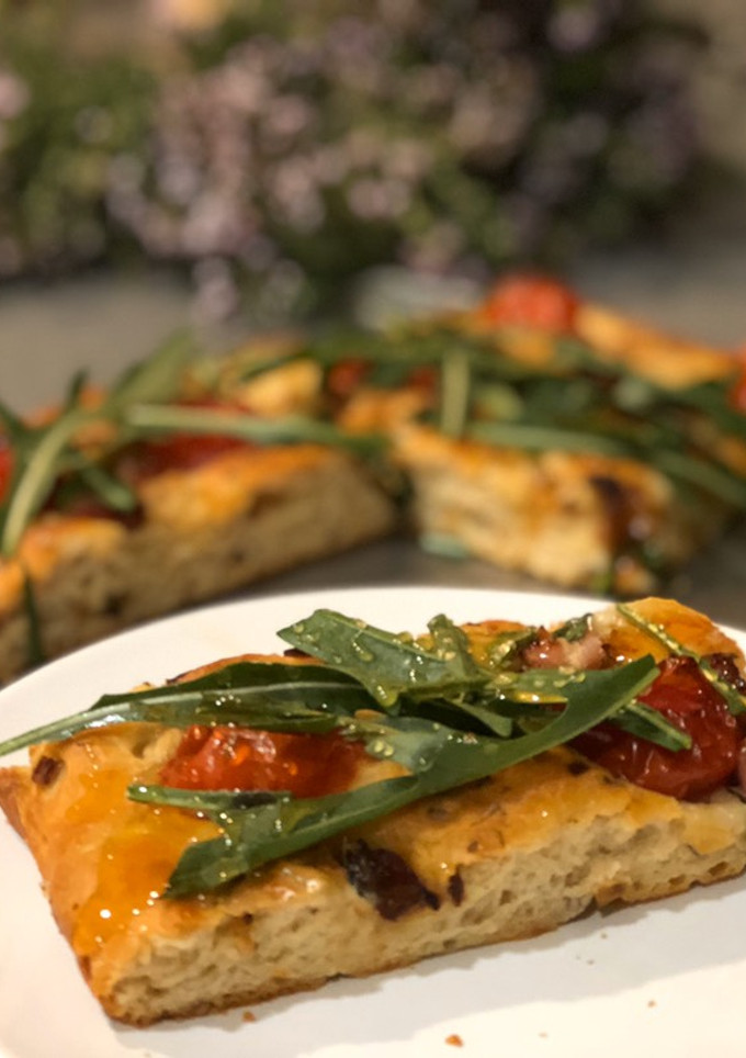 Una foto de Focaccia de cebolla y tomates cherry con rúcula