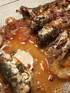 Una foto de Sardinas marinadas al horno, con fondo de tomates, cebollas, y patatas asadas