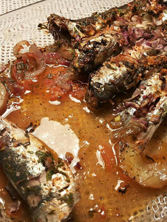 Una foto de Sardinas marinadas al horno, con fondo de tomates, cebollas, y patatas asadas